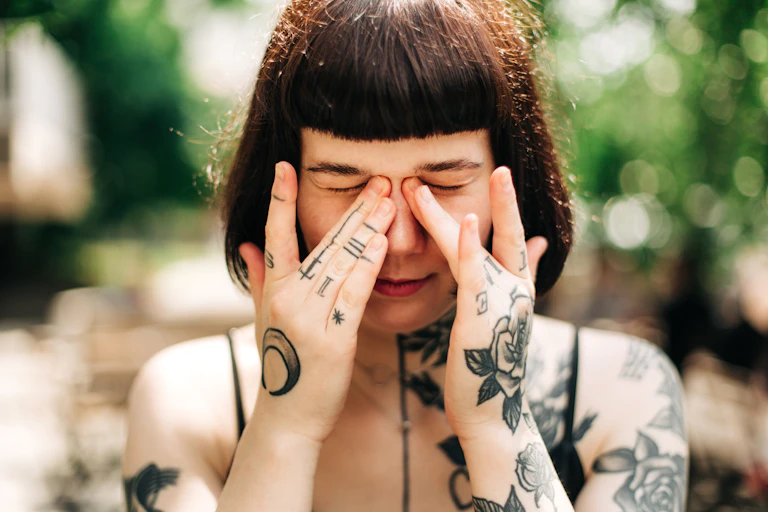 Young woman with multiple tattoos rubs eyes with her hands.