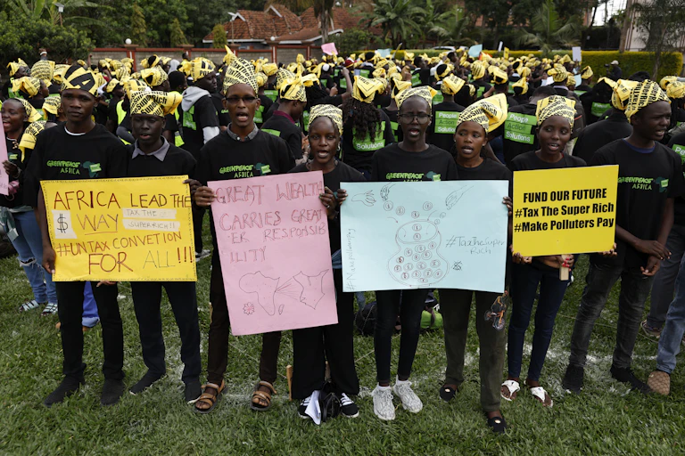 Protestors holding up placards reading 'Great Wealth Carries Greater Responsibility', 'Tax the Super Rich', 'Africa lead the way: UN Tax Convention for all'