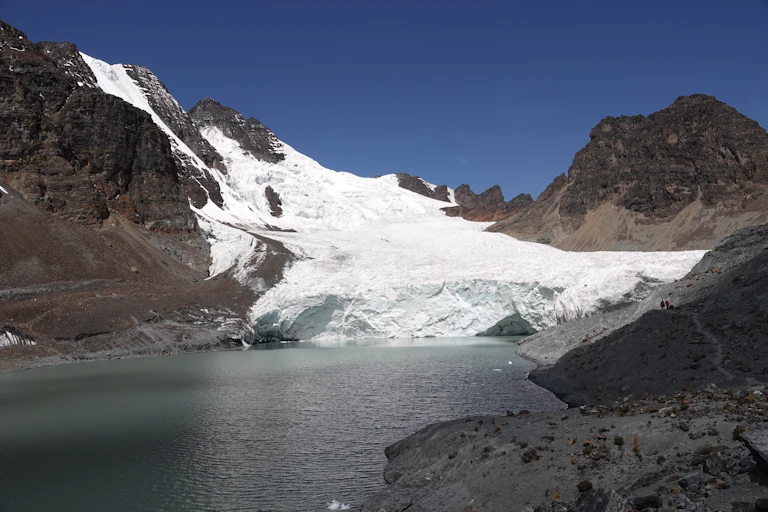 landscape with white glacier, stony mountains and greay water in foreground