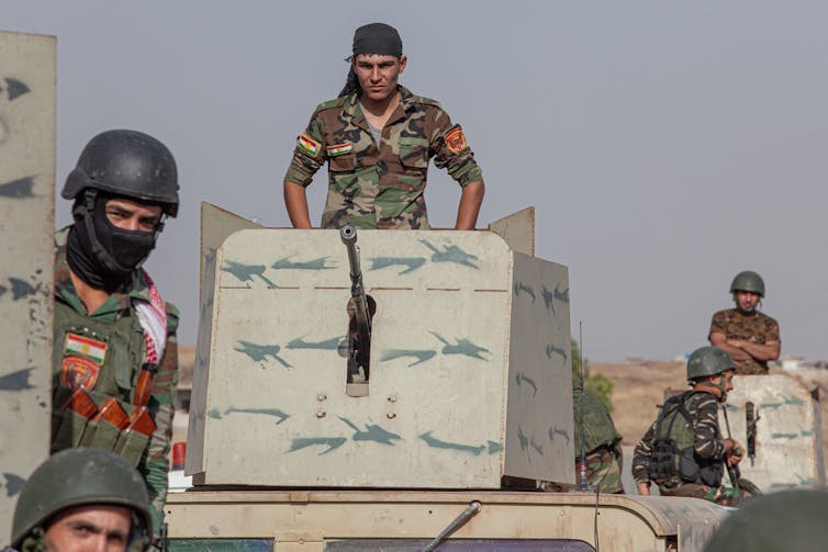 Kurdish fighters travel on the back of an armoured vehicle.