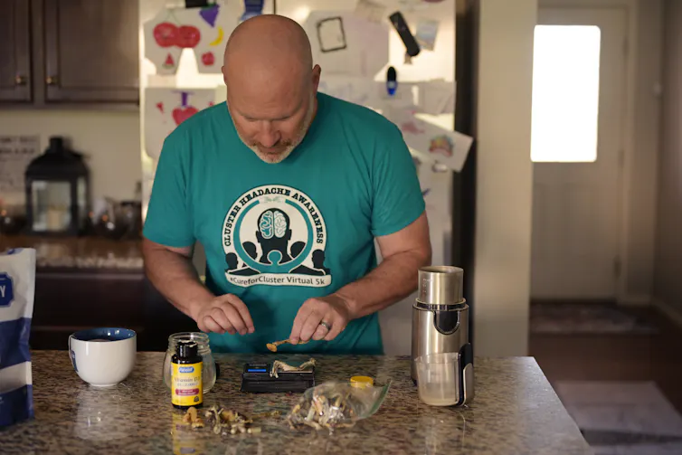A man in a blue shirt weighs mushrooms on a small scale in a kitchen.