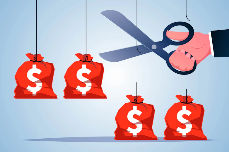 A man in a suit uses scissors to cut strings holding money bags up.