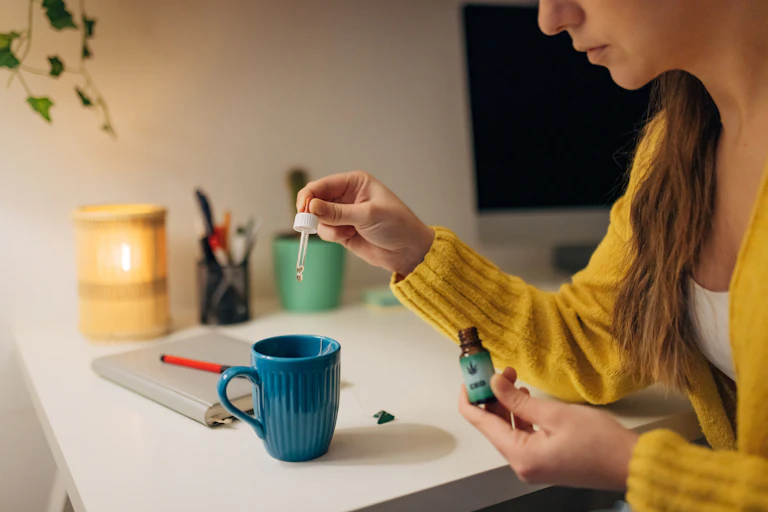Woman drops CBD oil into a cup of tea.