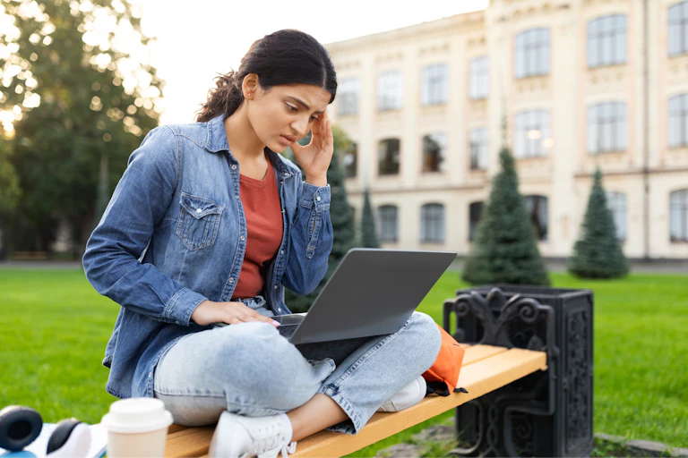Student outside looking worried on laptop