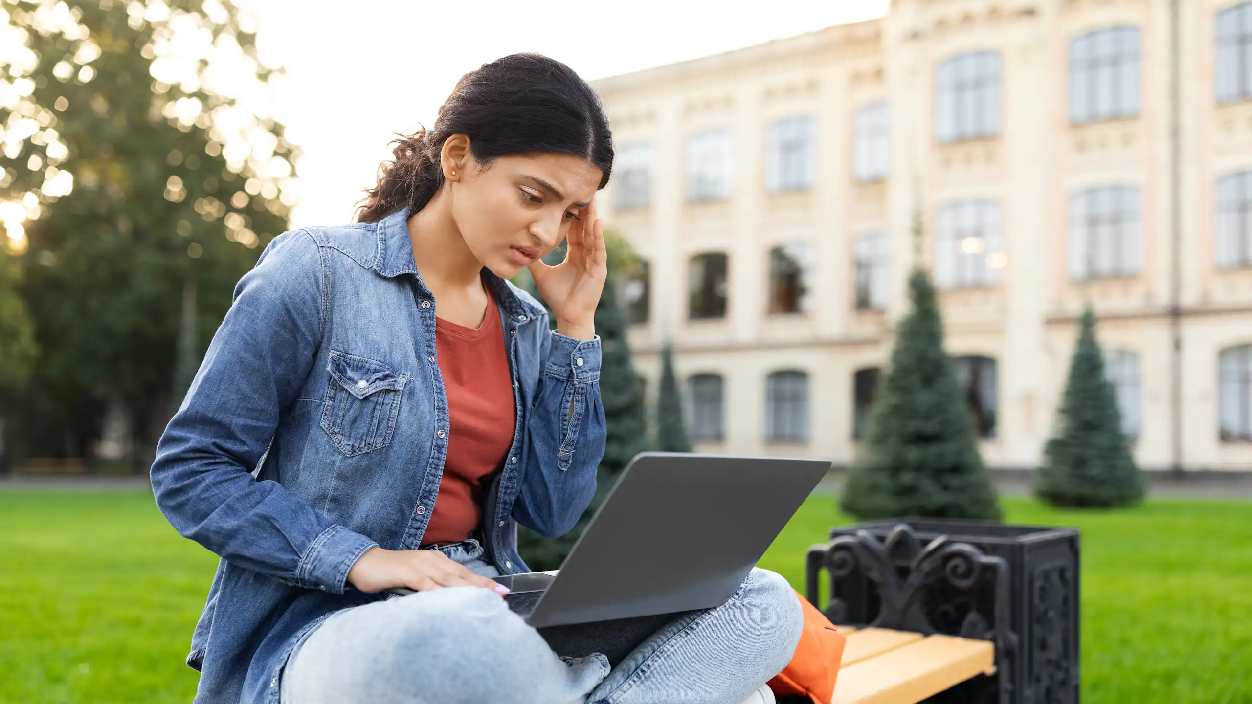 Student outside looking worried on laptop