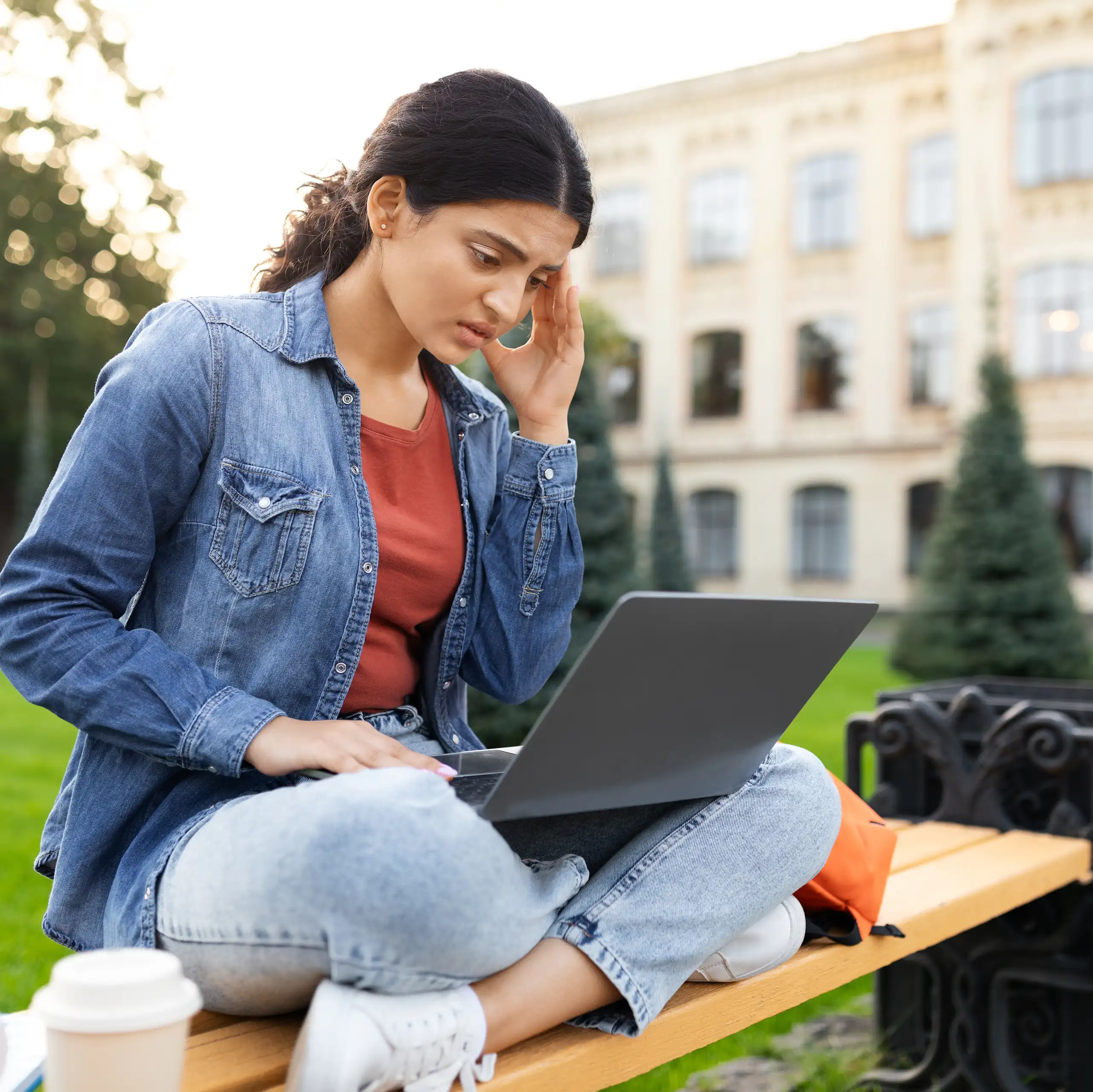 Student outside looking worried on laptop