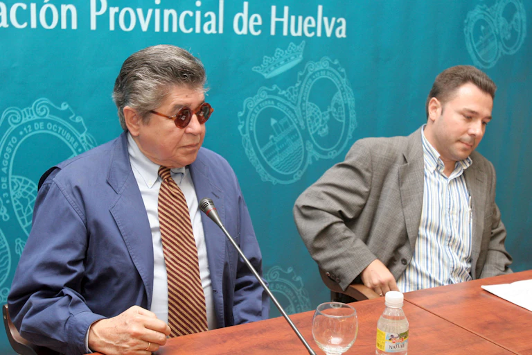 Un hombre con traje y gafas de sol a punto de hablar delante de un micro.