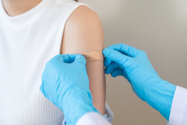 Hands in blue gloves putting plaster on woman's upper arm