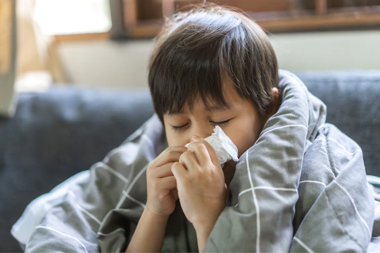 Child wrapped in duvet blowing nose