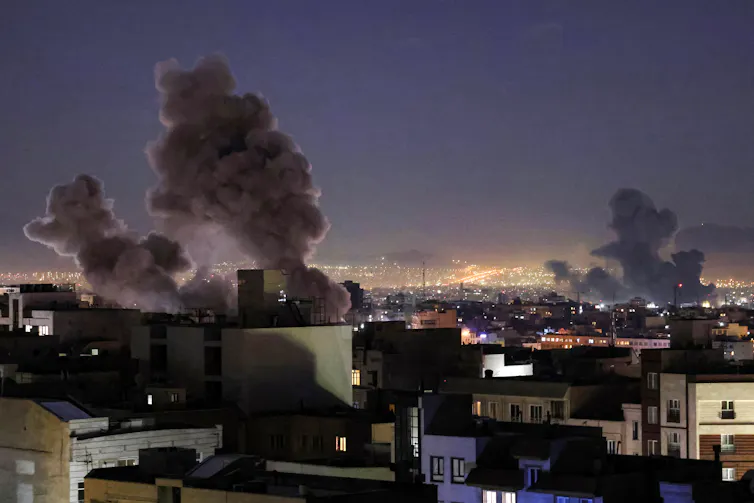 A view acros the city's rooftops with multiple large smoke plumes rising.