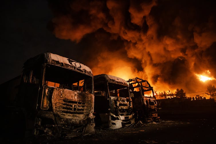Humo espeso y llamas sobre una hilera de camiones quemados.