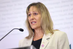 Una mujer de cabello rubio oscuro habla por un micrófono.