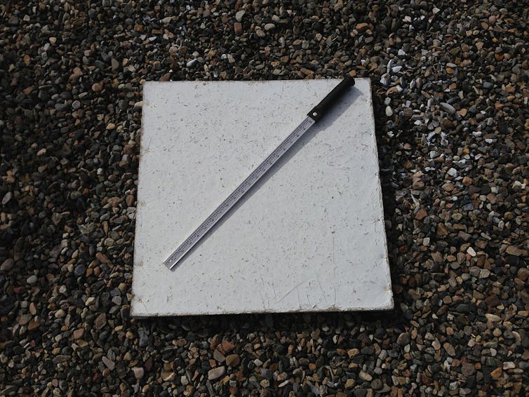 square white board with measuring stick lying across it on the ground