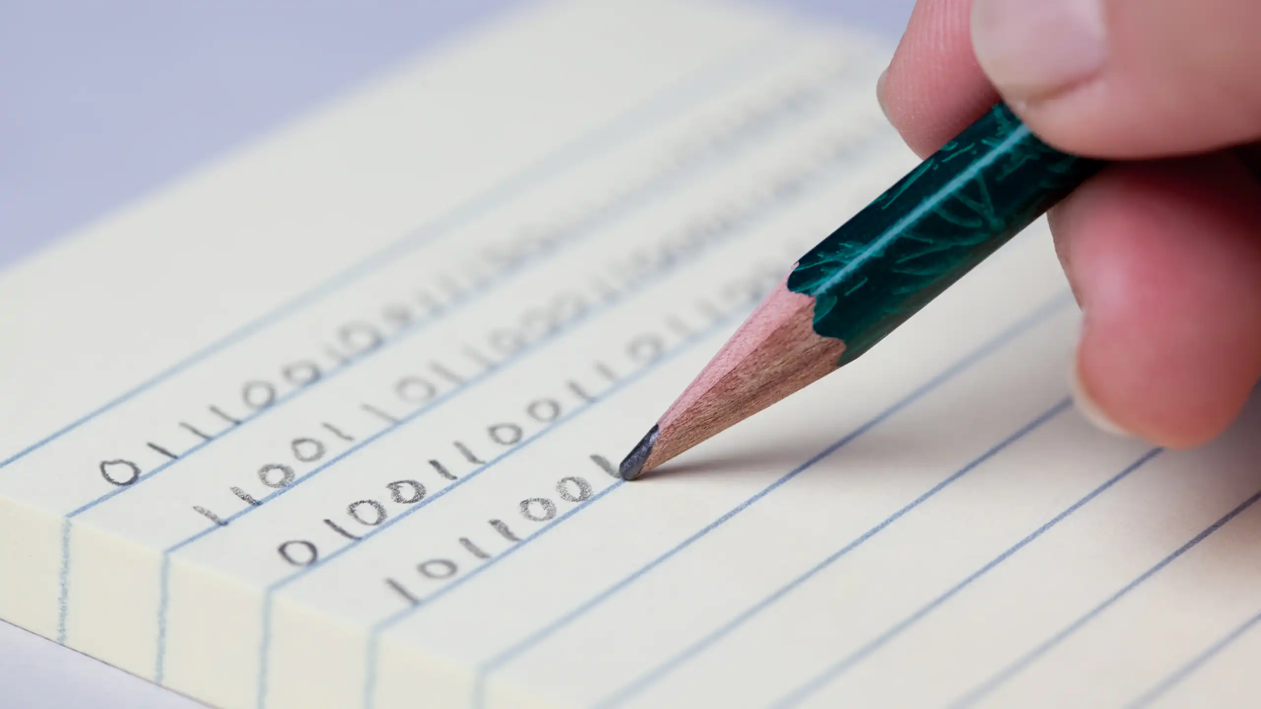 A hand holding a pencil and writing binary code on lined paper.