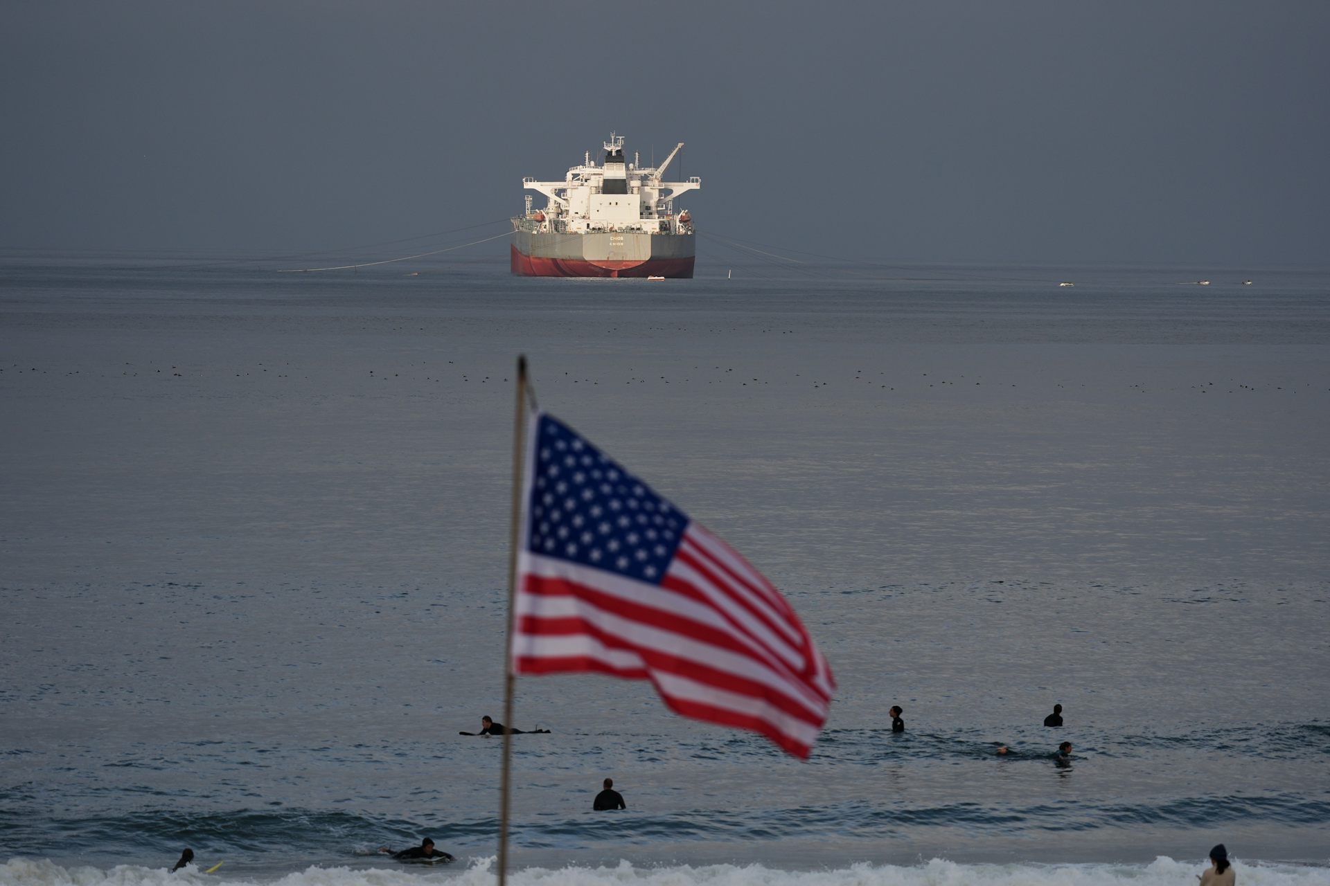 Una bandera estadounidense ondea en primer plano mientras un petrolero navega al fondo.