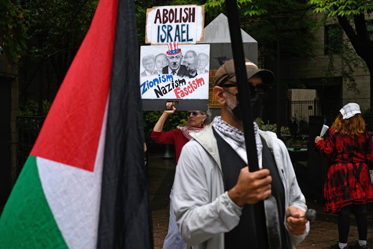 A protester holding signs picturing Israeli leader Benjamin Netanyahu with a Hitler mustache.