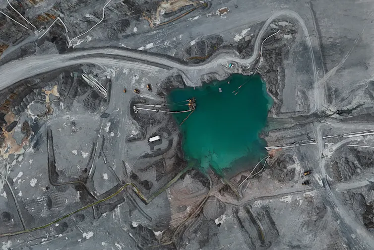 An aerial view of a large industrial operation with a water pit and gravel roads.