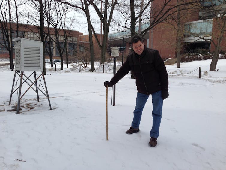 man leans on ruler poking into snow-covered ground
