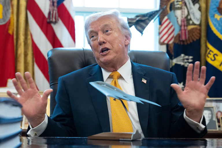 Donald Trump speaks from behind a desk with a model warplane on it