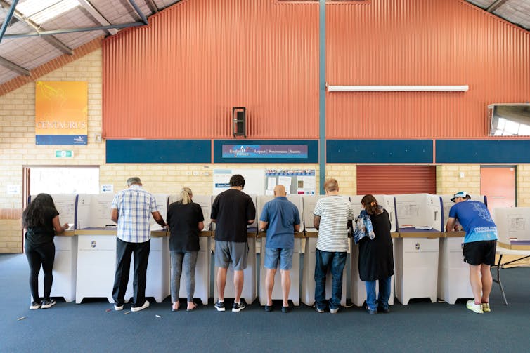 A line of people at cardboard voting booths in a school hall