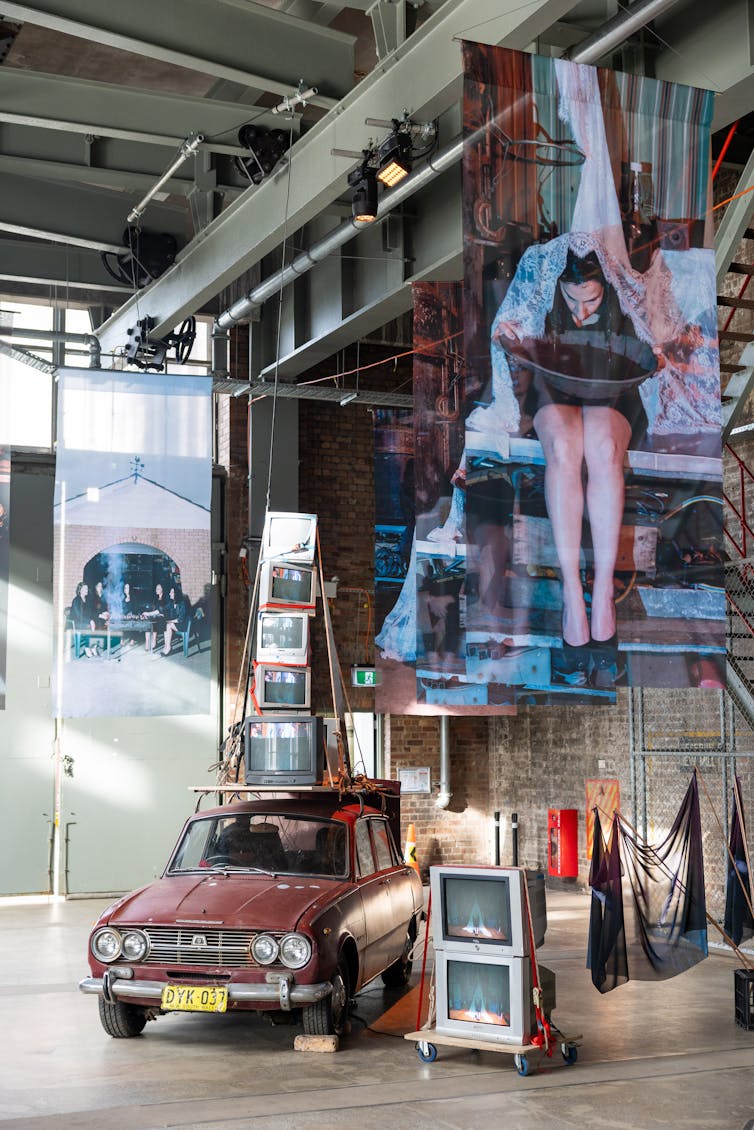 A car, some TVs, large hanging photos.