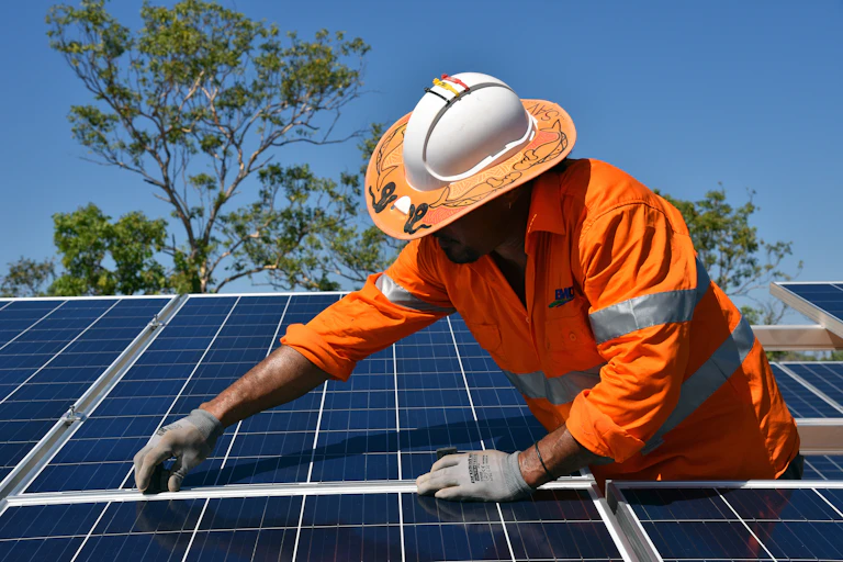 Man in orange hi-vis clothes and a hard hat installs a solar panel.