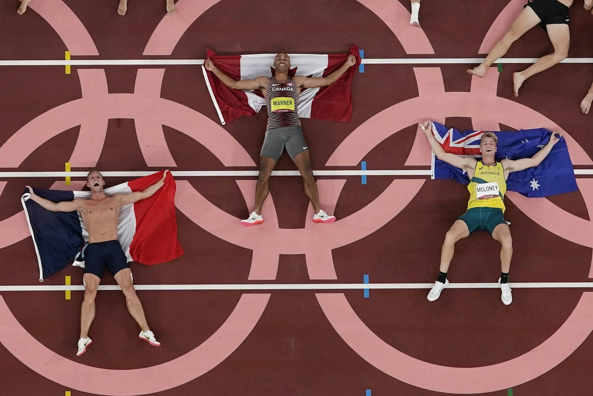 Three men with flags lying on a track inside the circles of the Olympic rings