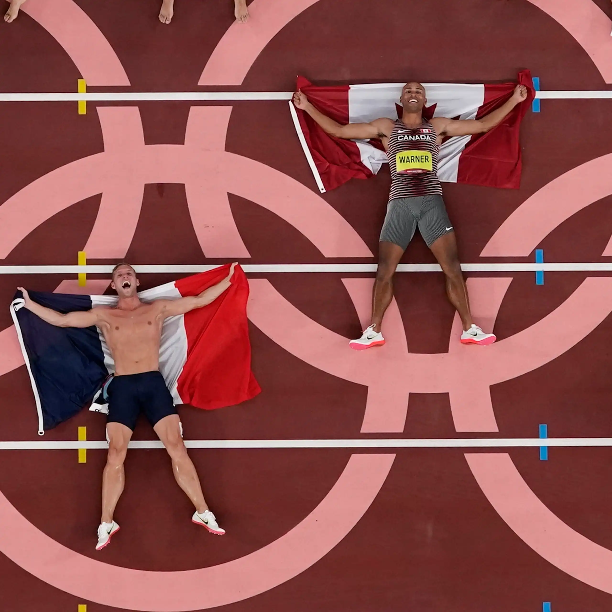Three men with flags lying on a track inside the circles of the Olympic rings