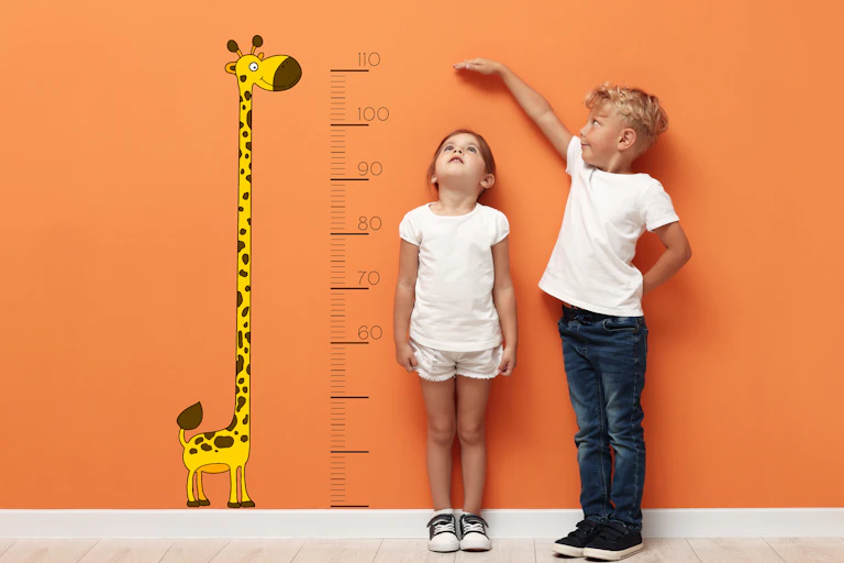 A girl and boy standing next to a height chart.