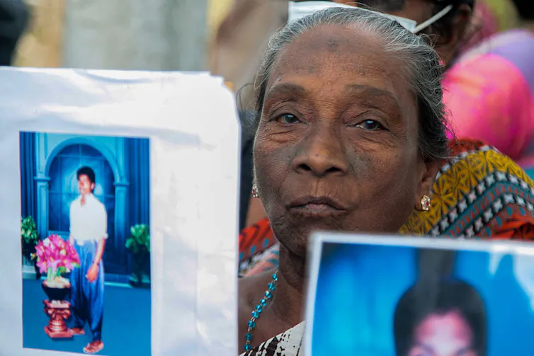 Rising up right through Sri Lanka’s civil battle taught me that obtaining in conjunction with other people throughout divides is a distinctive feature we will be informed 6 A woman with gray hair holds up a photograph of someone standing in front of a bright blue archway.