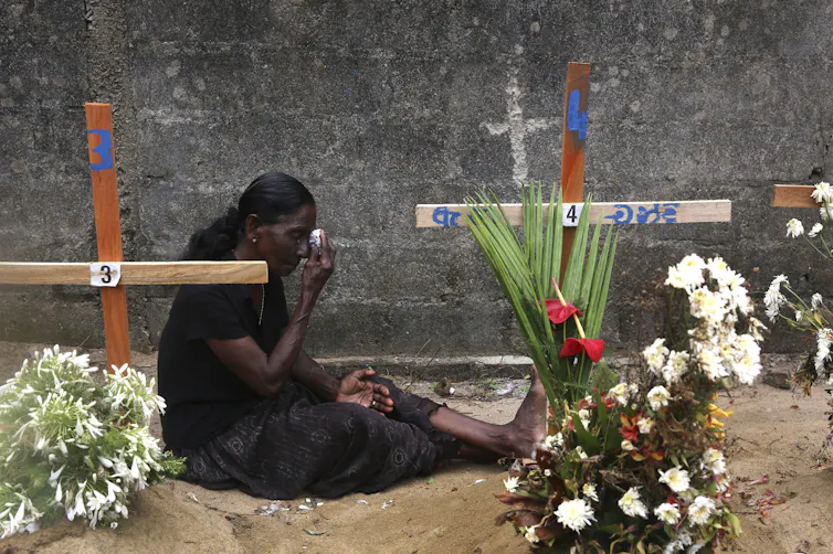 Rising up right through Sri Lanka’s civil battle taught me that obtaining in conjunction with other people throughout divides is a distinctive feature we will be informed 3 A woman wearing black wipes her eyes as she sits on the ground between graves marked with wooden crosses and flowers.