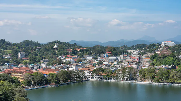 A view out over a city amid green hills, with a lake in the foreground.