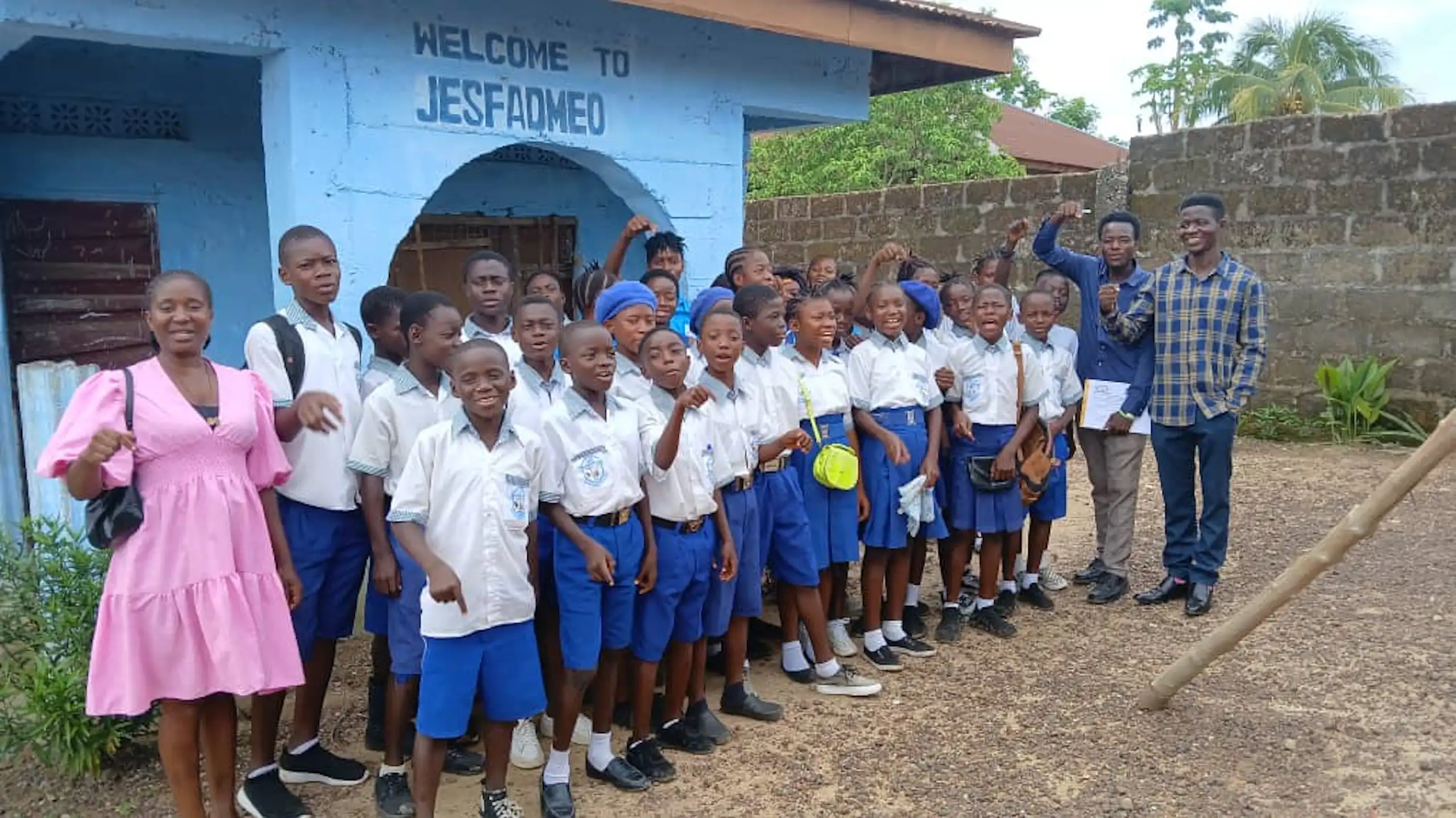About 30 young people in school uniform stand outside a blue building