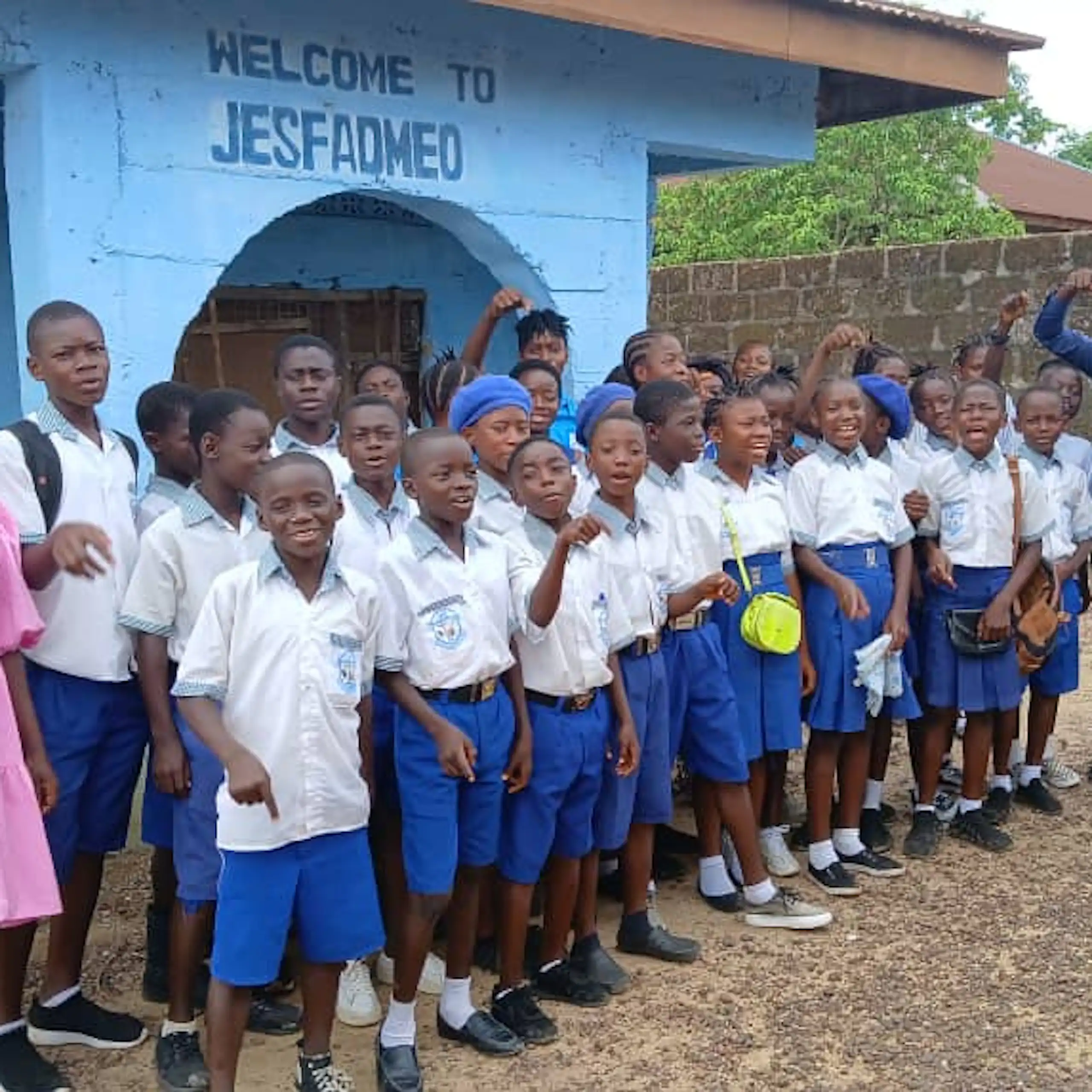About 30 young people in school uniform stand outside a blue building