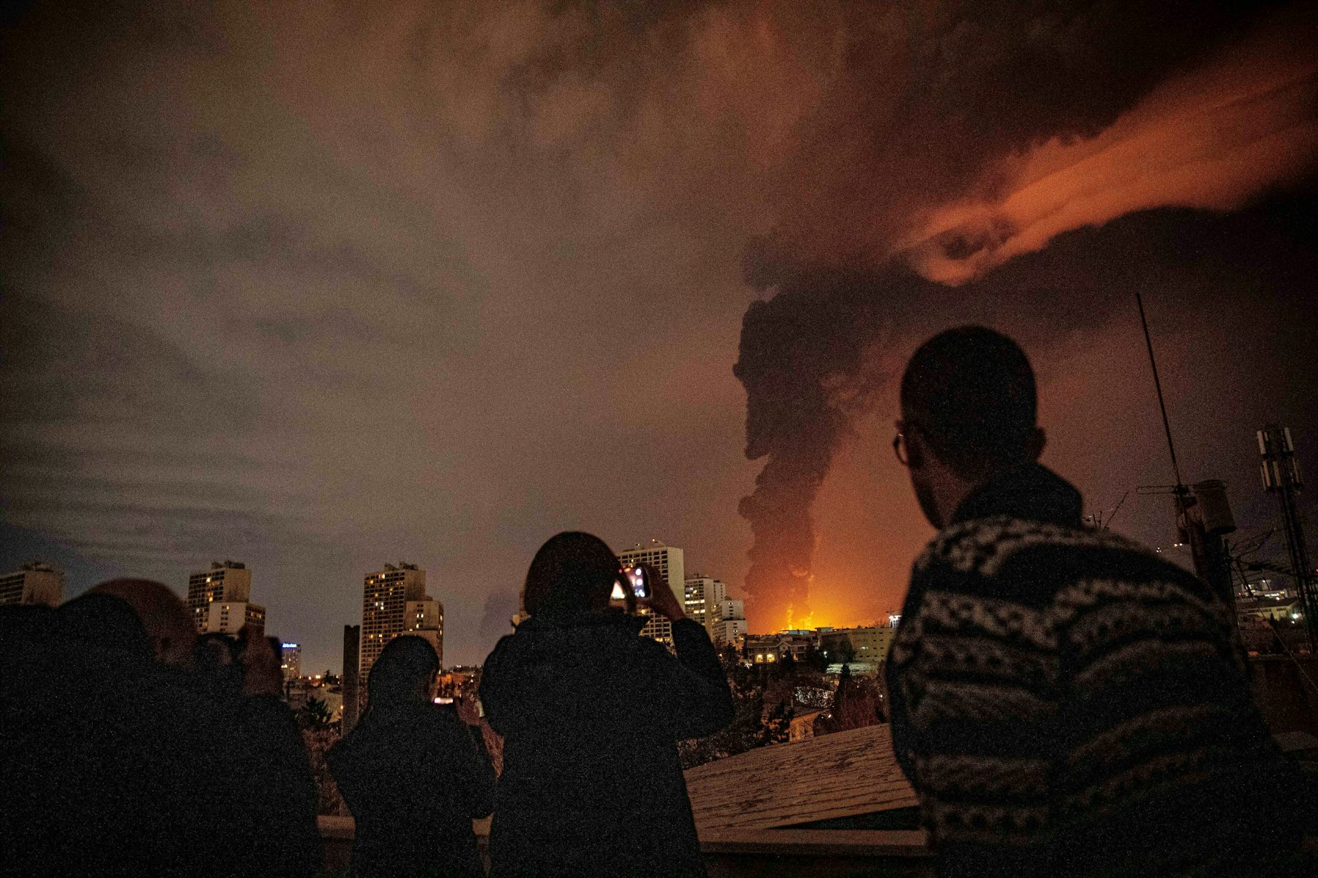 La gente observa cómo un gran incendio ilumina una zona oscura.