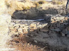 A wall of rocks piled on top of each other and held together by steel mesh, in a dry stream bed.