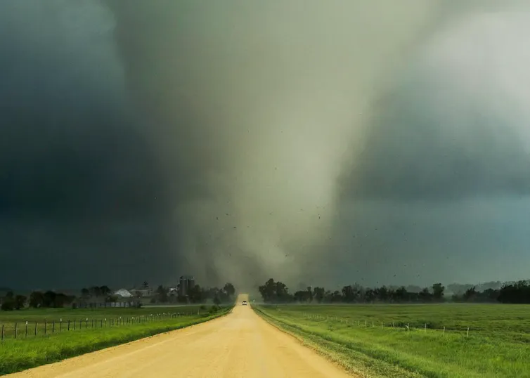 Um veículo desce por uma estrada rural, afastando-se de um grande tornado.