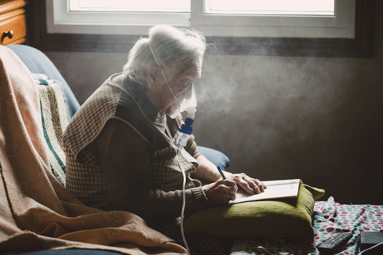 An older adult writes while using a machine with a face mask that assists with breathing.