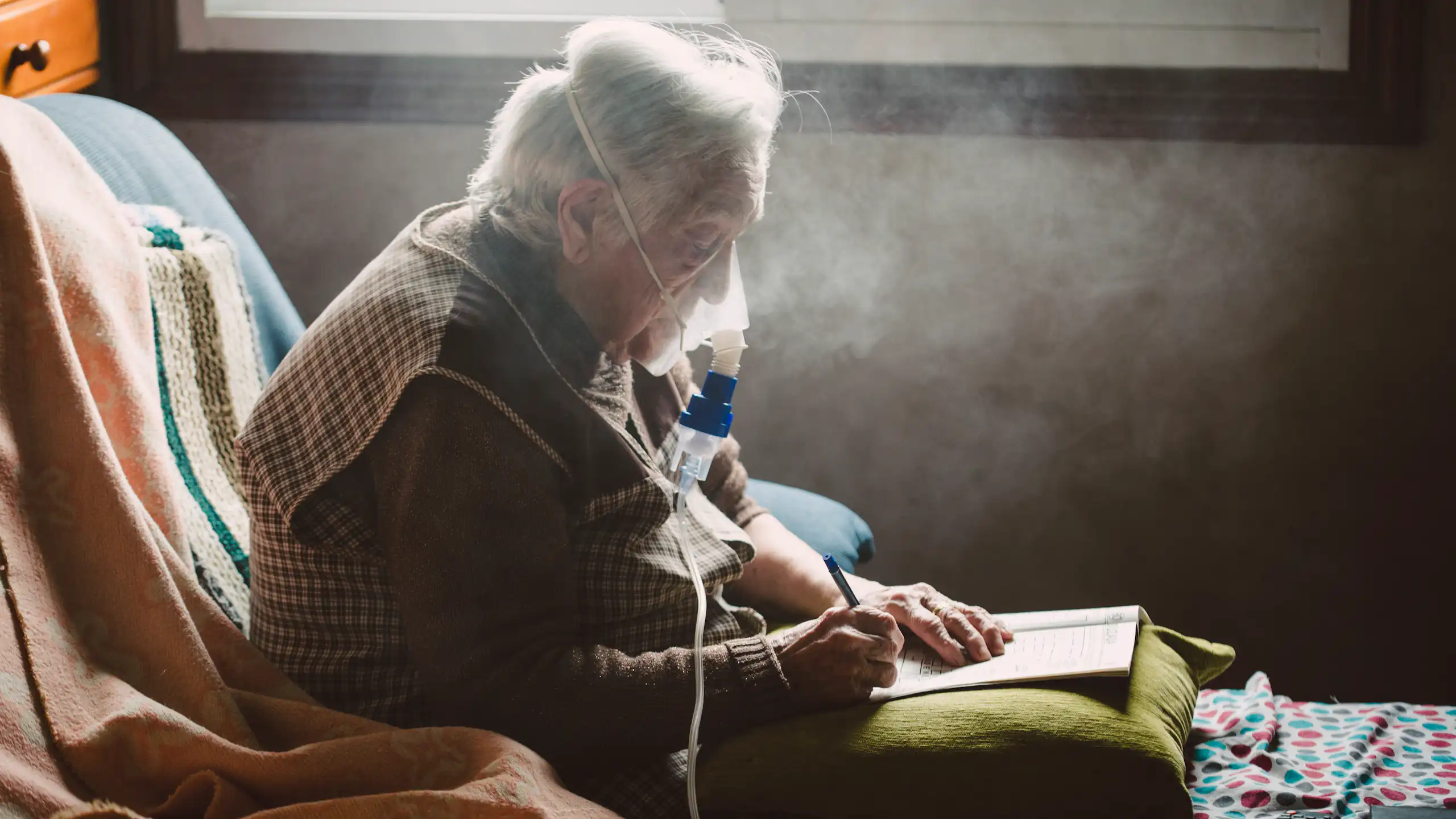 An older adult writes while using a machine with a face mask that assists with breathing.
