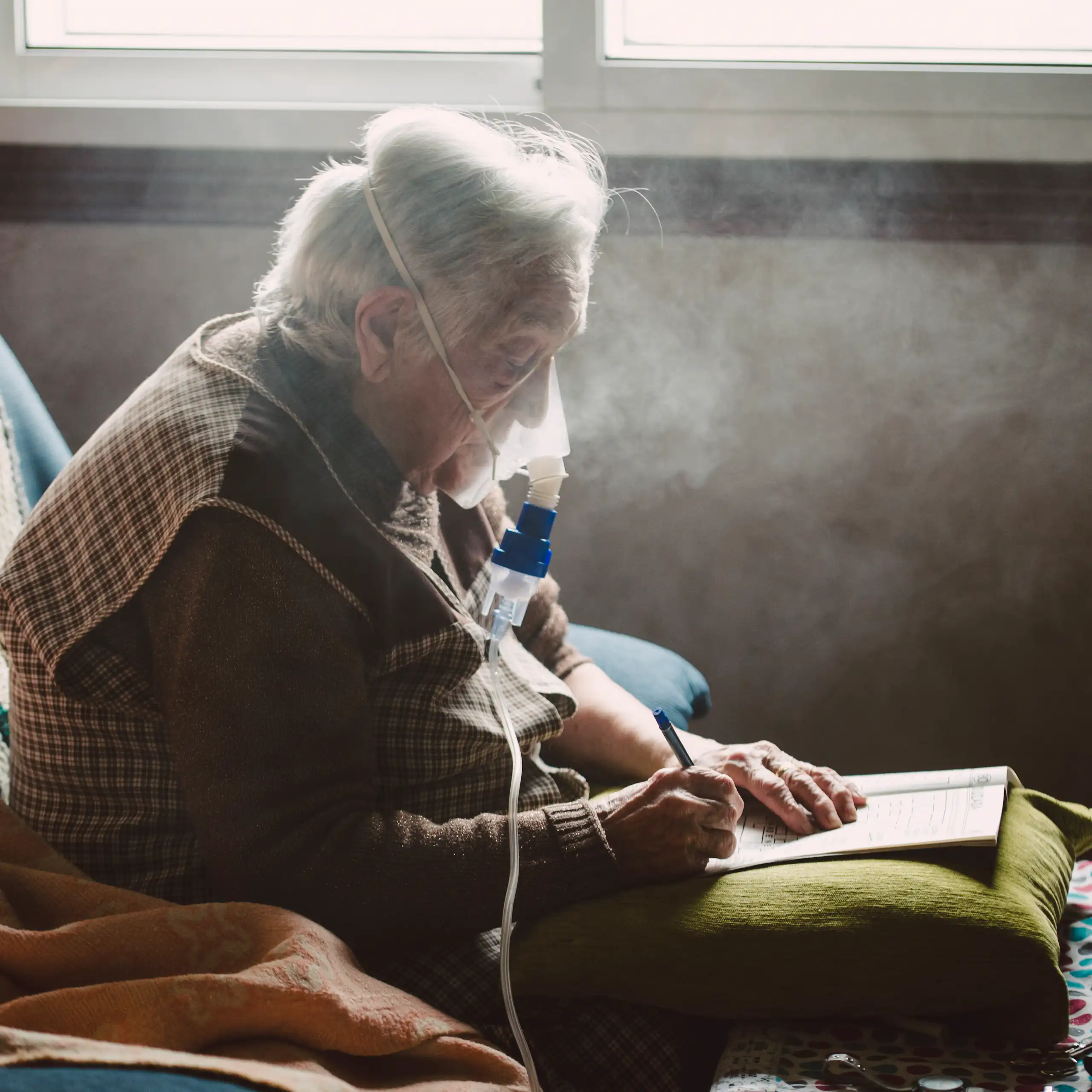 An older adult writes while using a machine with a face mask that assists with breathing.