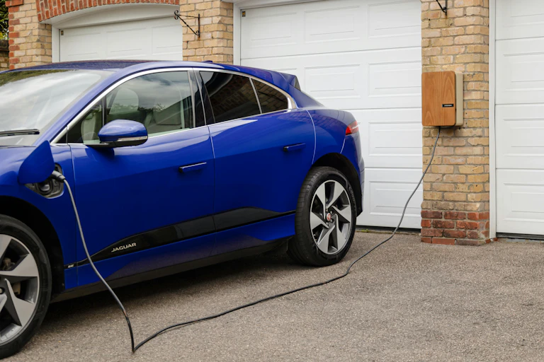 A blue car getting charged at home outside a garage