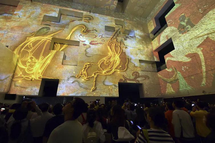 Digital screens in a museum display artistic images in various shades of yellow and orange.