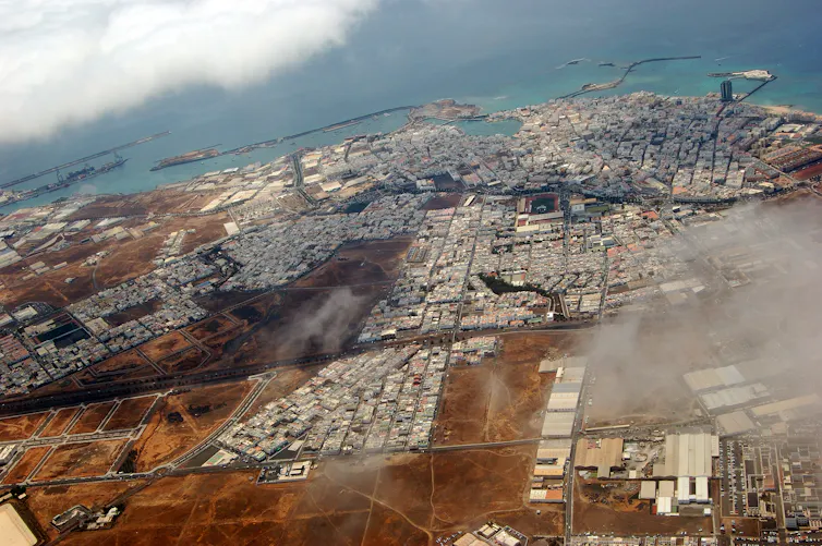 Un ciudad costera con edificios blancos y rodeada de terreno yermo vista desde el cielo