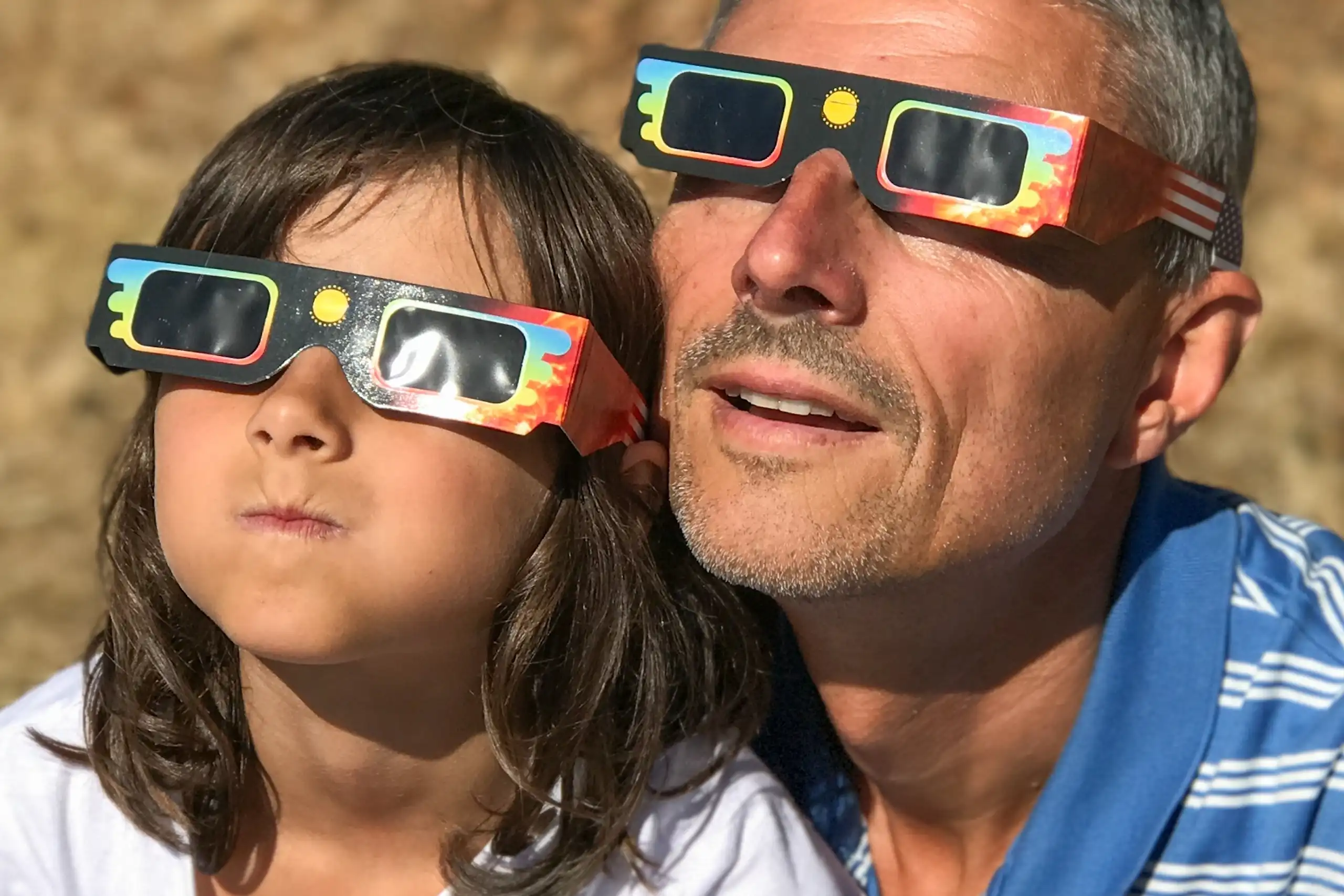 Un home i una xiqueta miren al cel amb ulleres de sol de cartró.