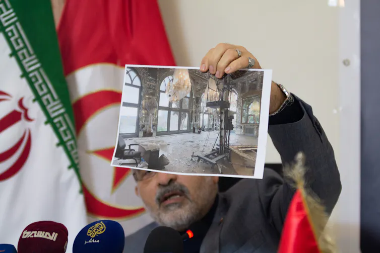 Un hombre sostiene una fotografía de un sitio patrimonial dañado en una conferencia de prensa.