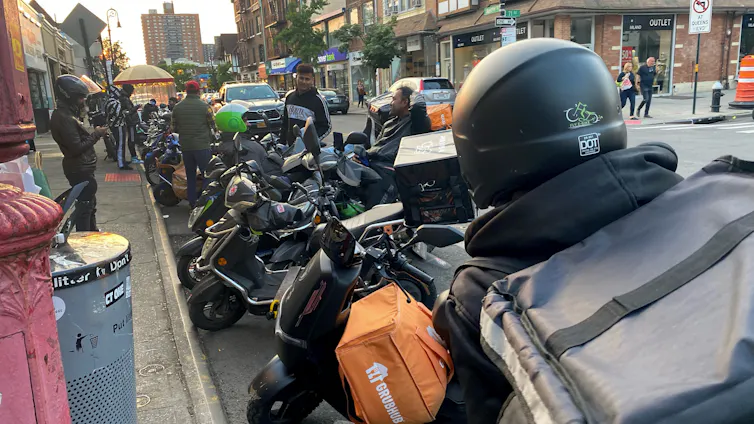 A big group of delivery workers people seen on a street with their motorcycles.