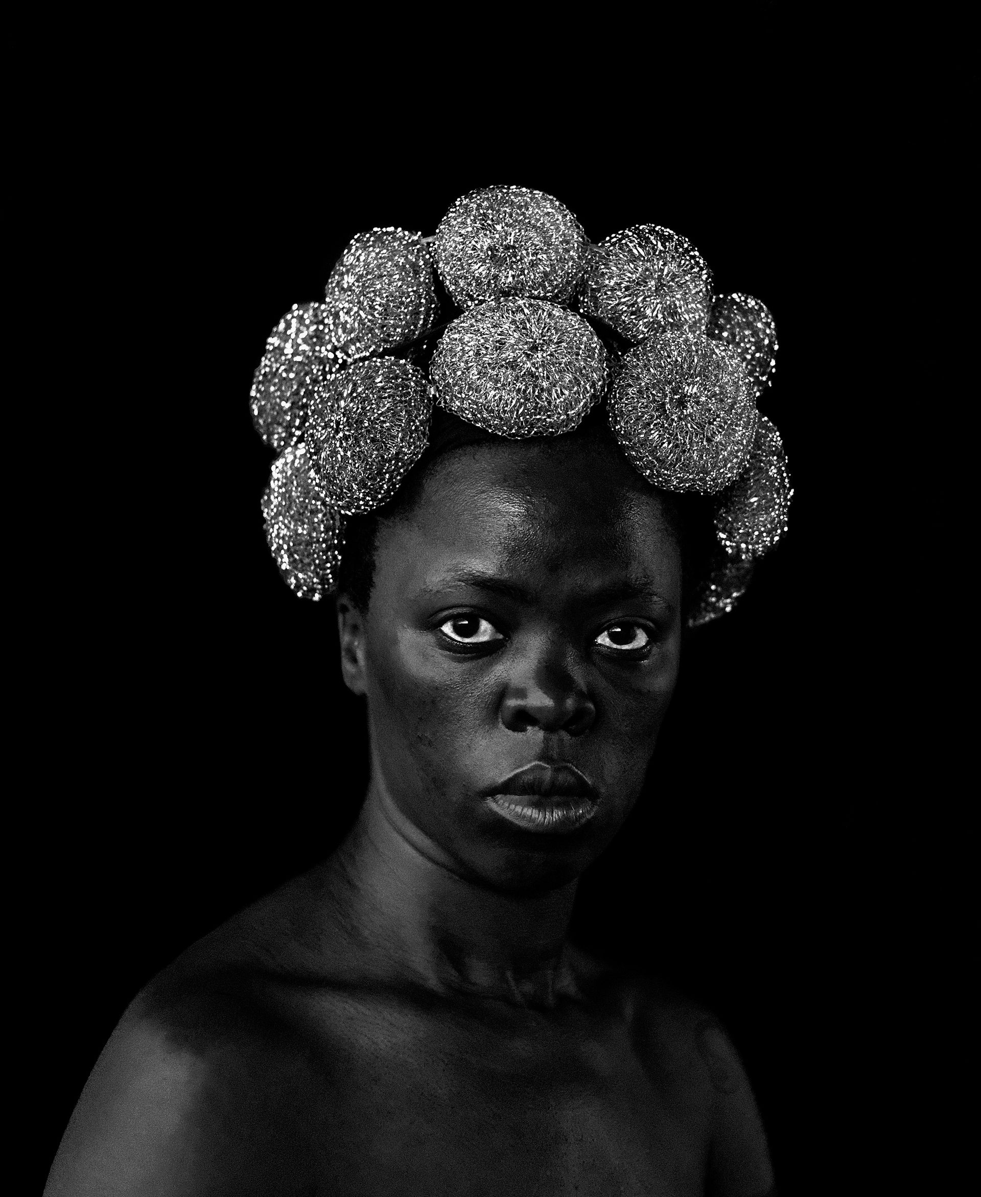 An African woman stares straight at camera, her hair made up of steel wool rolls.