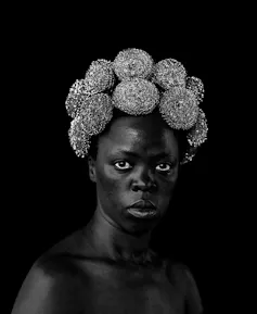 An African woman stares straight at camera, her hair made up of steel wool rolls.