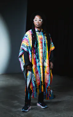 An African person is depicted wearing white glasses and a colourful cloak