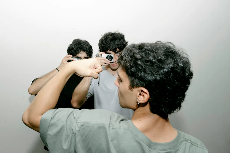 A young man flexing while two others are taking photographs of him.